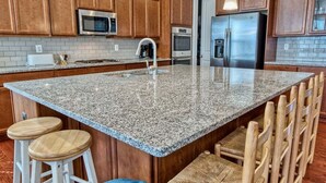Una cocina con encimeras de granito, armarios de madera, electrodomésticos de acero inoxidable y taburetes de bar.