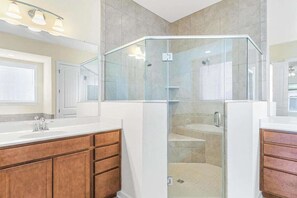 A modern bathroom with a glass-enclosed shower, a white vanity, and a large mirror.