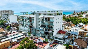 A modern multi-story building with balconies, located in a coastal urban area with a view of the sea. - Simply Splendid - Centrally Located, Amazing Pool/Gym! (Puerto Vallarta)