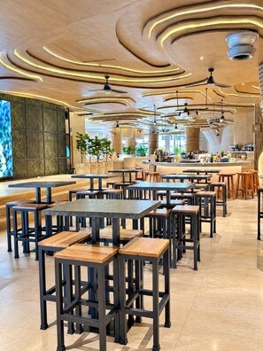 Un interior de restaurante moderno con varias mesas y sillas, una zona de bar y ventiladores de techo.