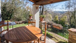 An outdoor patio with a wooden table and chairs, surrounded by potted plants and a stone wall.