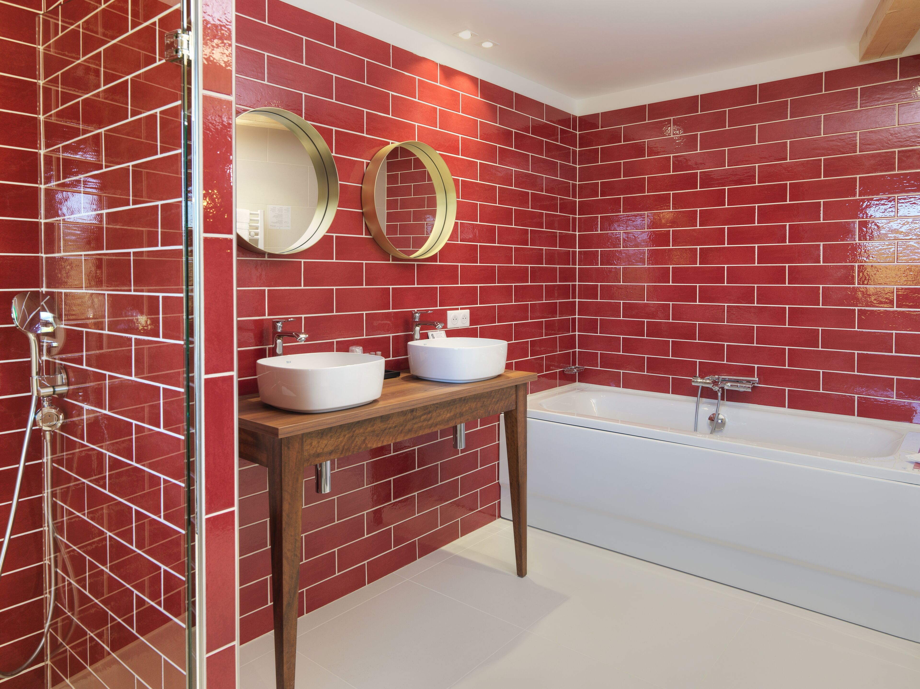 Une salle de bain avec des murs recouverts de carreaux rouges, deux lavabos, une baignoire et deux miroirs.