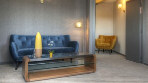 A modern living room with a blue sofa, a glass coffee table, a yellow vase, and a yellow armchair. - Hotel Les Grains D'argent (Dizy)
