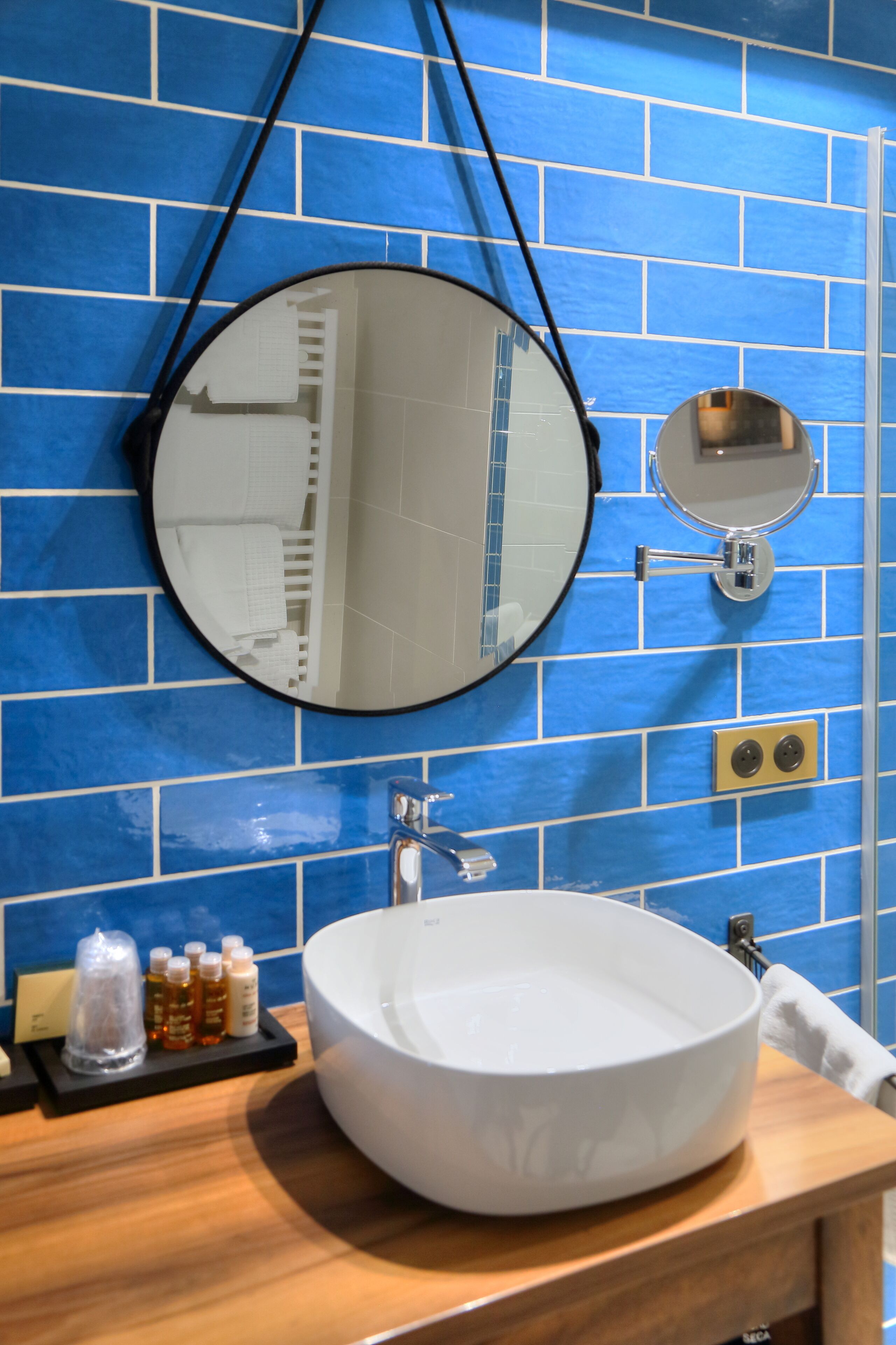 A bathroom with a large white sink, two round mirrors, and a blue-tiled wall.