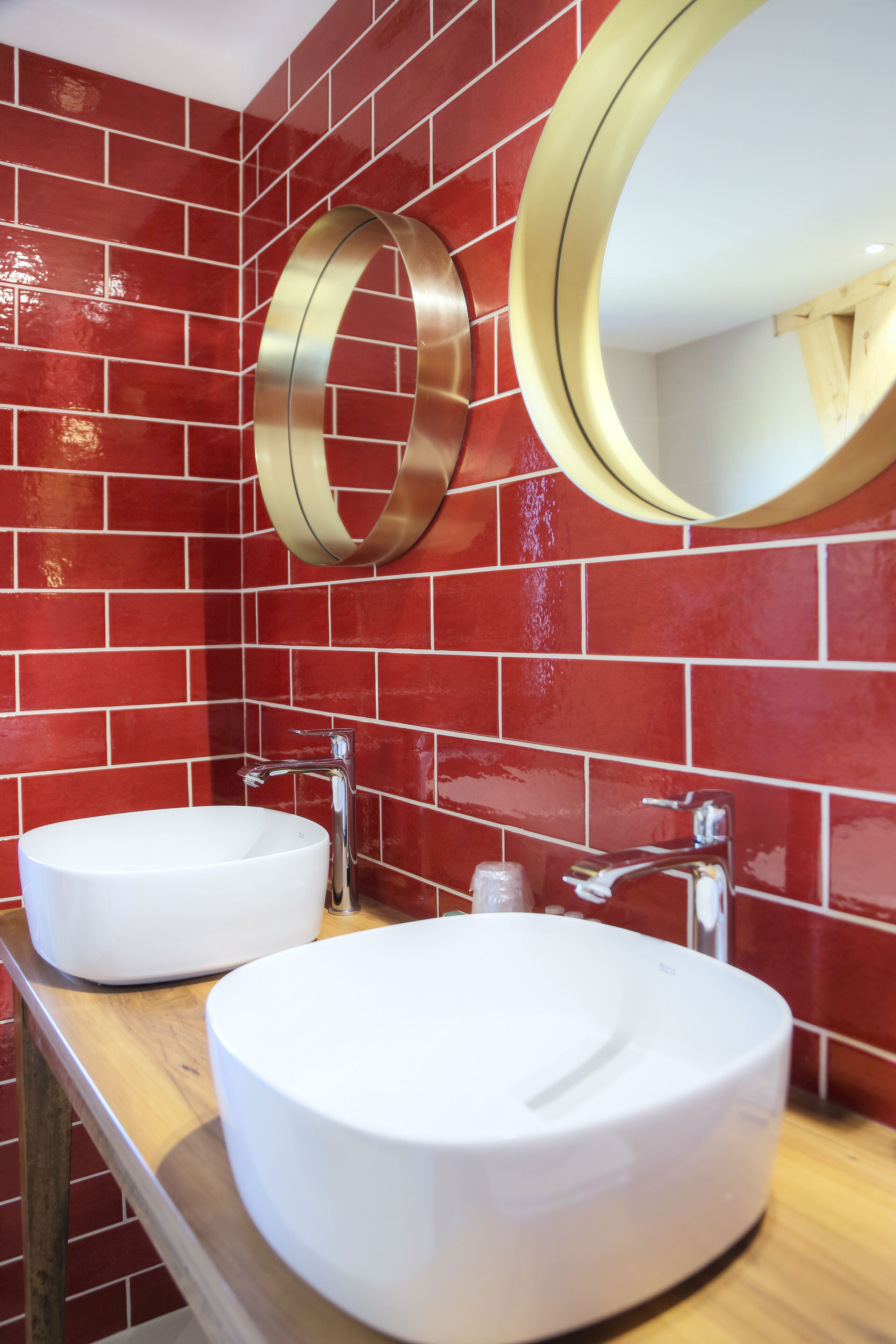 A bathroom with two white sinks, a wooden countertop, and red-tiled walls.