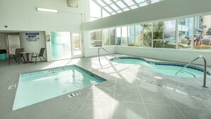 Una piscina interior con techos de vidrio transparente, un cartel de socorrista y vistas al exterior.