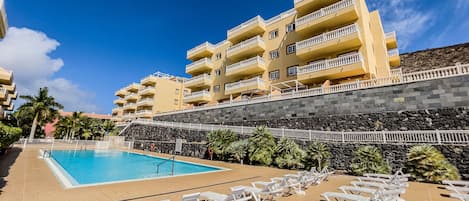 Um hotel com piscina, espreguiçadeiras brancas e um muro de pedra.