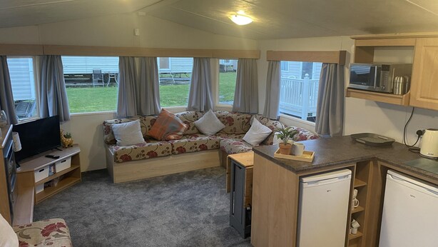 A compact RV interior with a sofa, kitchenette, and a TV. - Charming 3-bed Static Caravan in Porthcawl (Porthcawl)