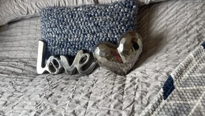 A bed with a quilted blanket, a blue knitted pillow, and decorative metal letters spelling "Love" with heart-shaped accents. - Charming 3-bed Static Caravan in Porthcawl (Porthcawl)