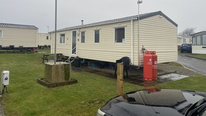 A mobile home with a small porch, a gas cylinder, and a water tank. - Charming 3-bed Static Caravan in Porthcawl (Porthcawl)