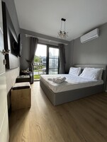 Una habitación de hotel moderna con una cama grande, un escritorio pequeño, un televisor de pantalla plana y un balcón con vistas a la ciudad.