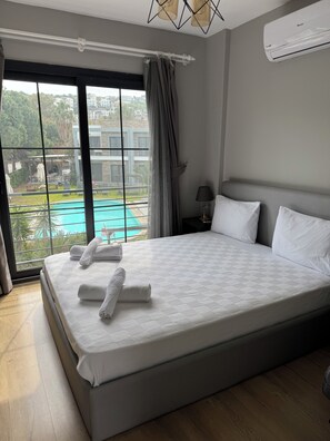 A hotel room with a large bed, a view of a swimming pool, and an air conditioning unit. - Malta Bodrum (Bodrum)