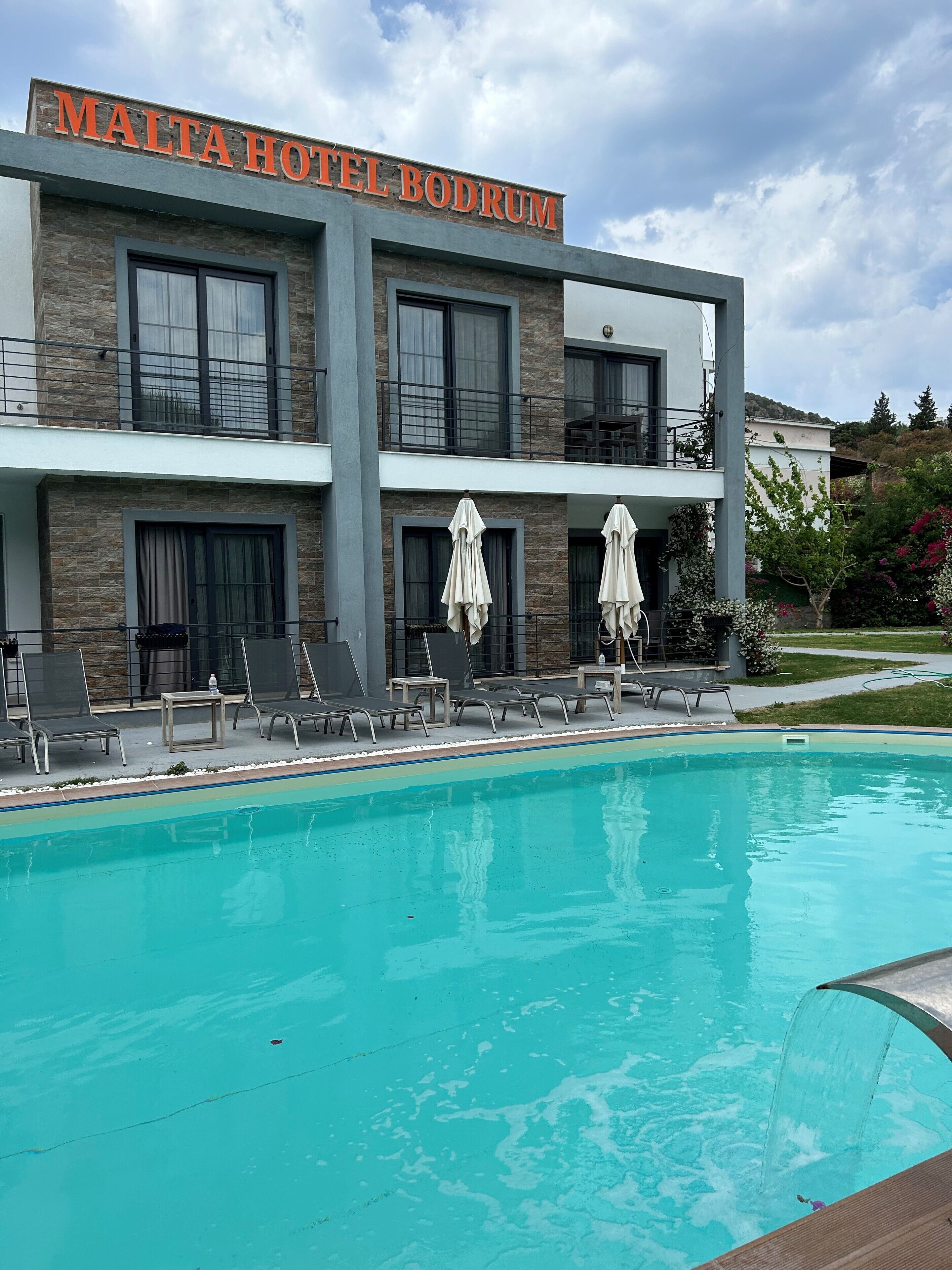 A hotel with a pool, outdoor seating, and a sign reading "MALTA HOTEL BODRUM".