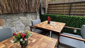 An outdoor dining area with a wooden table and chairs, a decorative centerpiece, and a thatched wall.