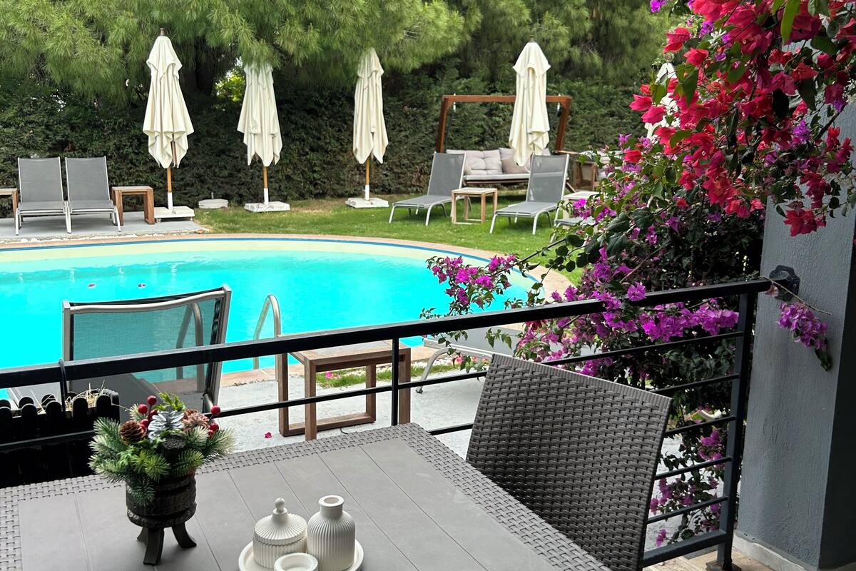 A patio with a pool, outdoor seating, and a table with a vase of flowers.
