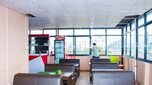 A restaurant with a view of the city, featuring a counter with a Coca-Cola refrigerator, several tables, and chairs. - Hotel om (Kathmandu)