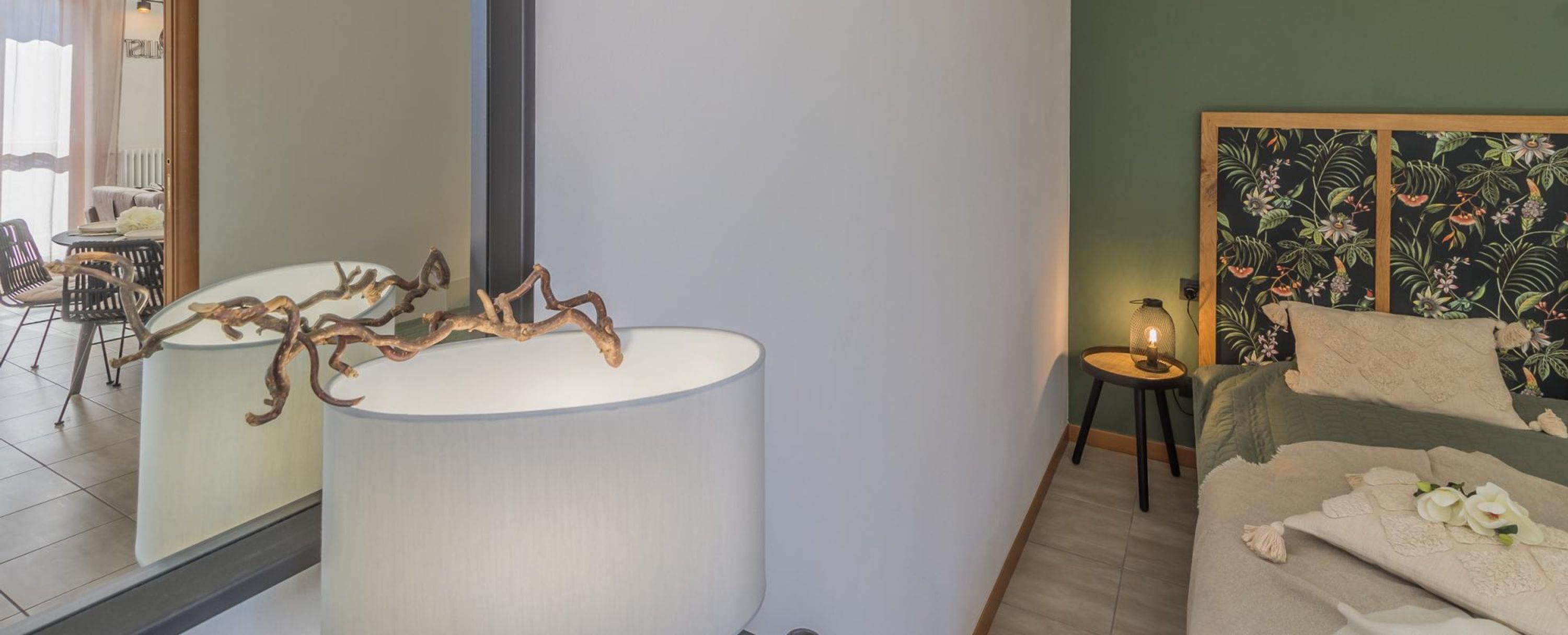 A modern living room with a sofa, a coffee table with a branch decoration, a lamp, and a wall with a floral pattern.