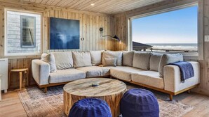 A cozy living room with a large sectional sofa, a round coffee table, and a view of the ocean. - Daydreamer - Beachfront! (Cannon Beach)