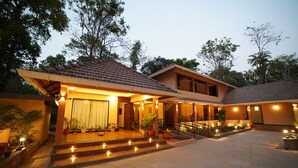 A two-story house with a tiled roof, a staircase leading to the entrance, and outdoor lighting. - Aananda wellness and resorts (Beltangadi)
