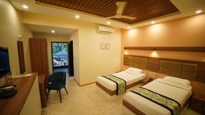 A hotel room with two beds, a desk, a chair, and a ceiling fan. - Aananda wellness and resorts (Beltangadi)