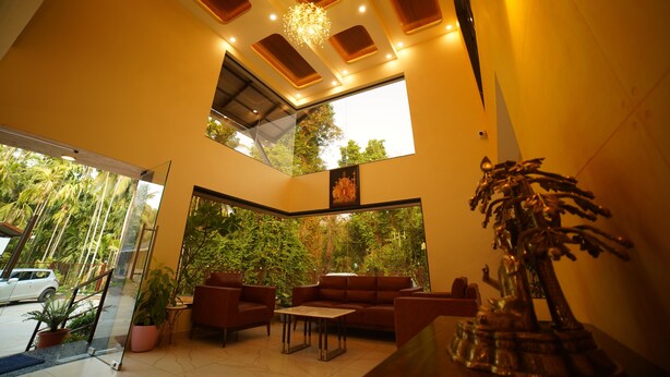 A modern interior with a high ceiling, large windows, and a seating area with a sofa and table. - Aananda wellness and resorts (Beltangadi)