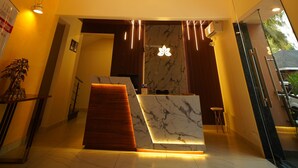 A modern hotel lobby with a marble reception desk, wooden accents on the ceiling, and a chandelier. - Aananda wellness and resorts (Beltangadi)