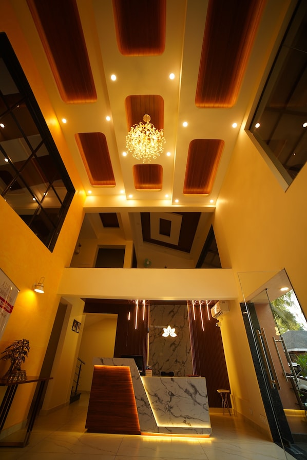 Un moderno vestíbulo de hotel con mostrador de recepción de mármol, detalles de madera en el techo y un candelabro.