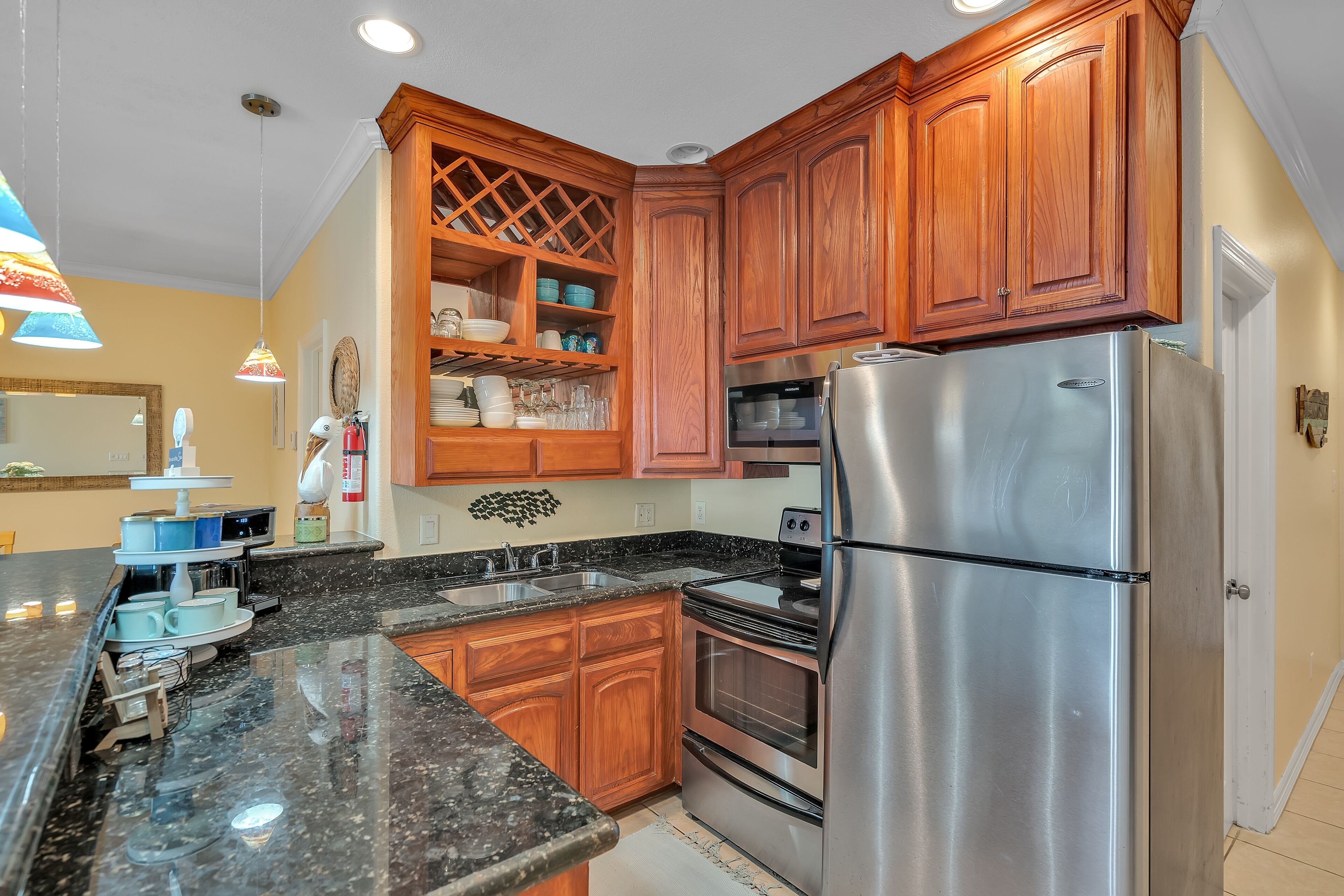 A kitchen with wooden cabinets, a stainless steel refrigerator, a double oven, granite countertops, and a built-in wine rack.