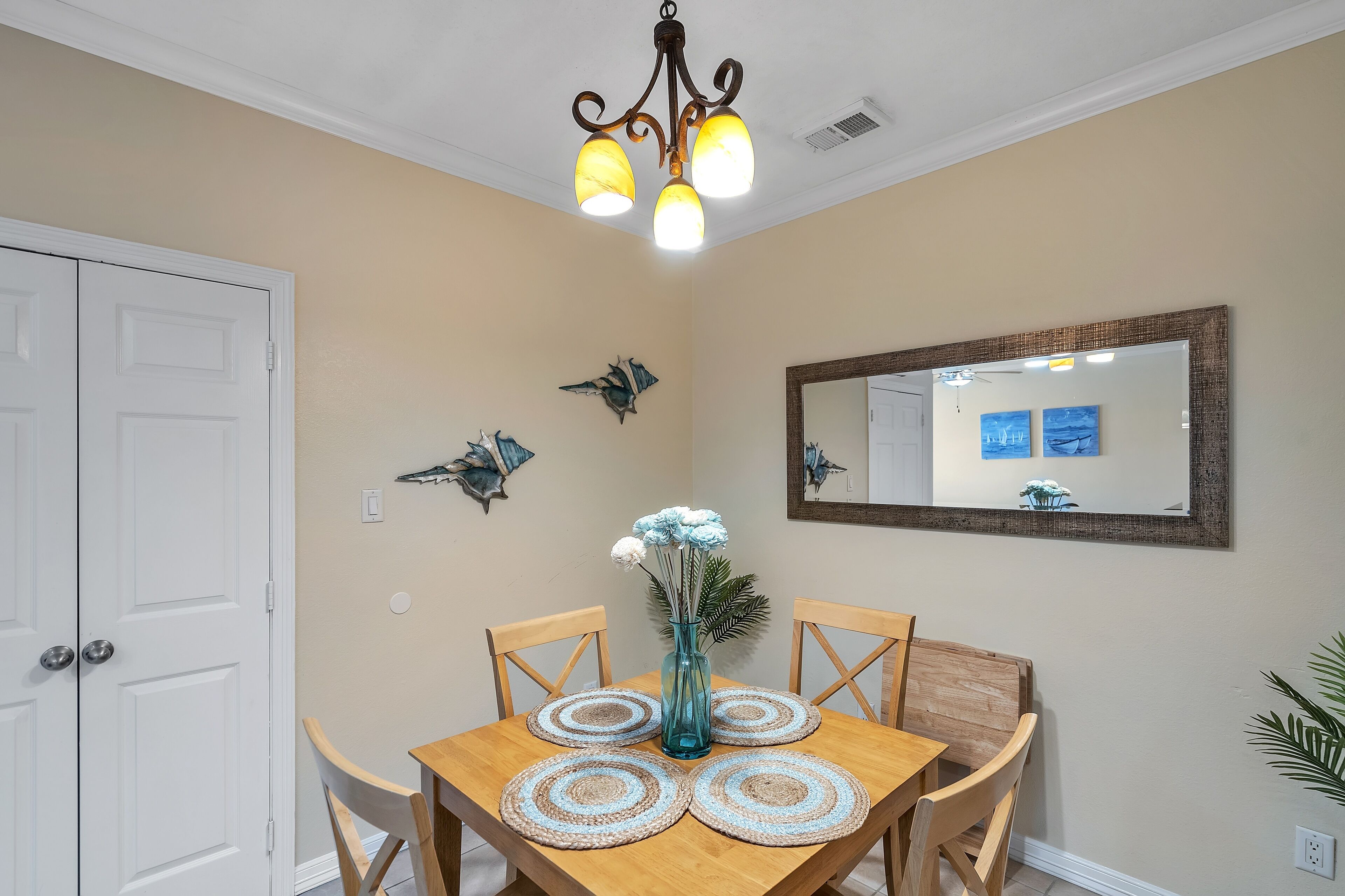 A dining area with a wooden table, four chairs, a vase with flowers, and wall art.