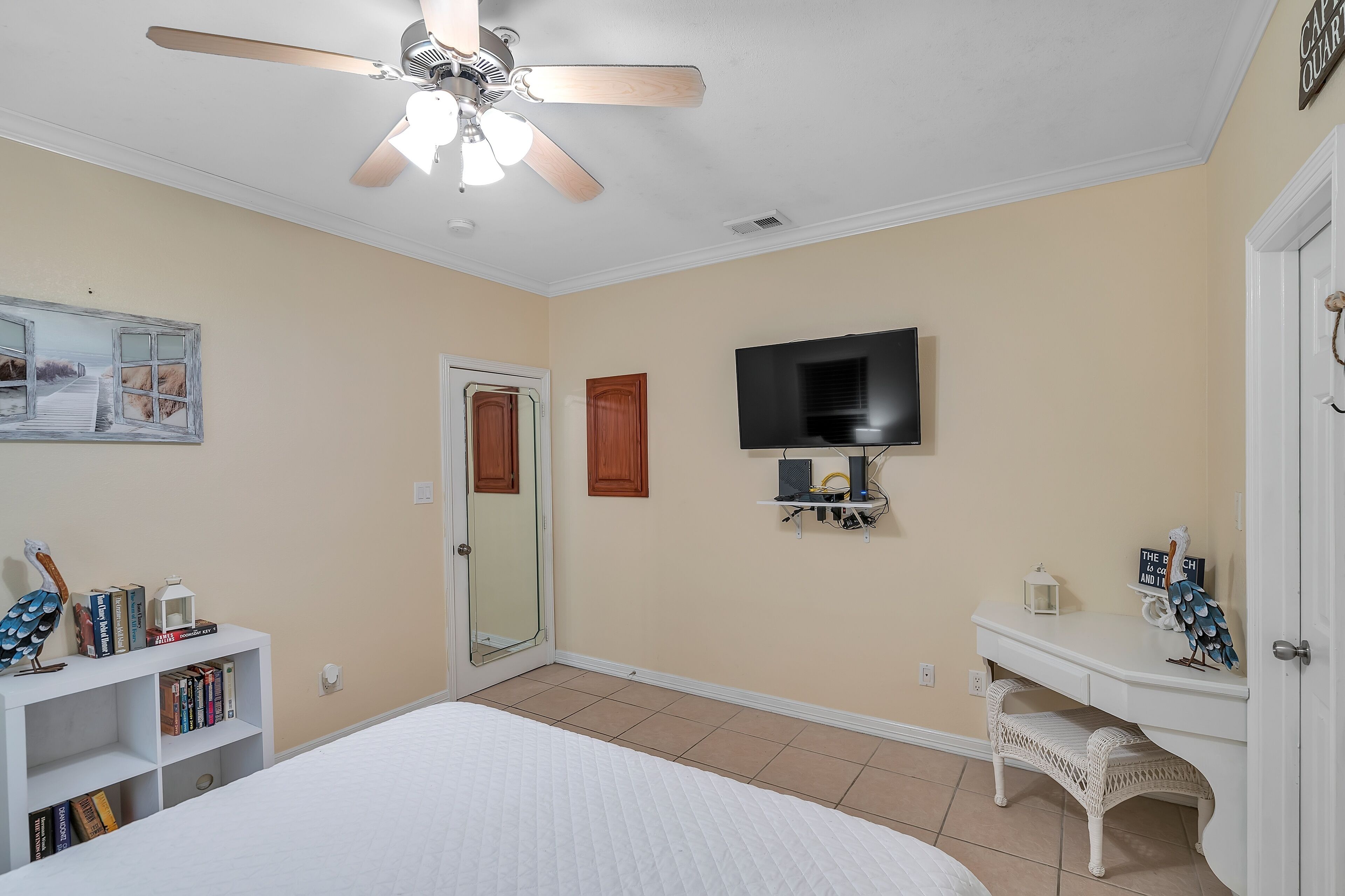 A bedroom with a bed, a ceiling fan, a TV, a bookshelf, and a door.