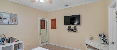 A bedroom with a bed, a ceiling fan, a TV, a bookshelf, and a door.