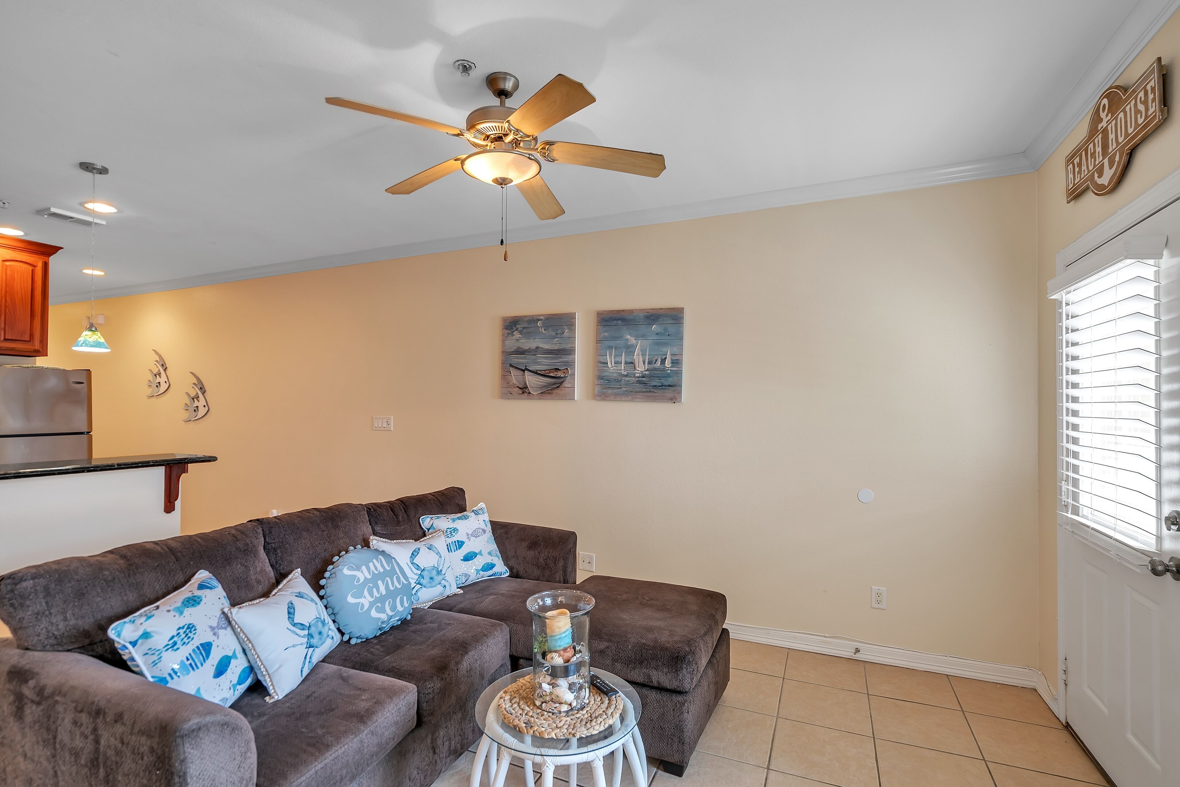 A living room with a brown sofa, a ceiling fan, and wall art.