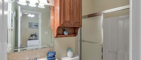 A bathroom with a white sink, a mirror, a wooden cabinet, and a shower enclosure.