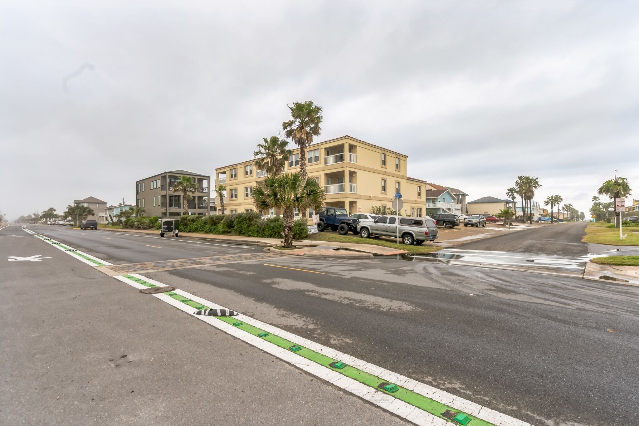 Un edificio residencial de varios pisos con balcones, coches aparcados y palmeras.
