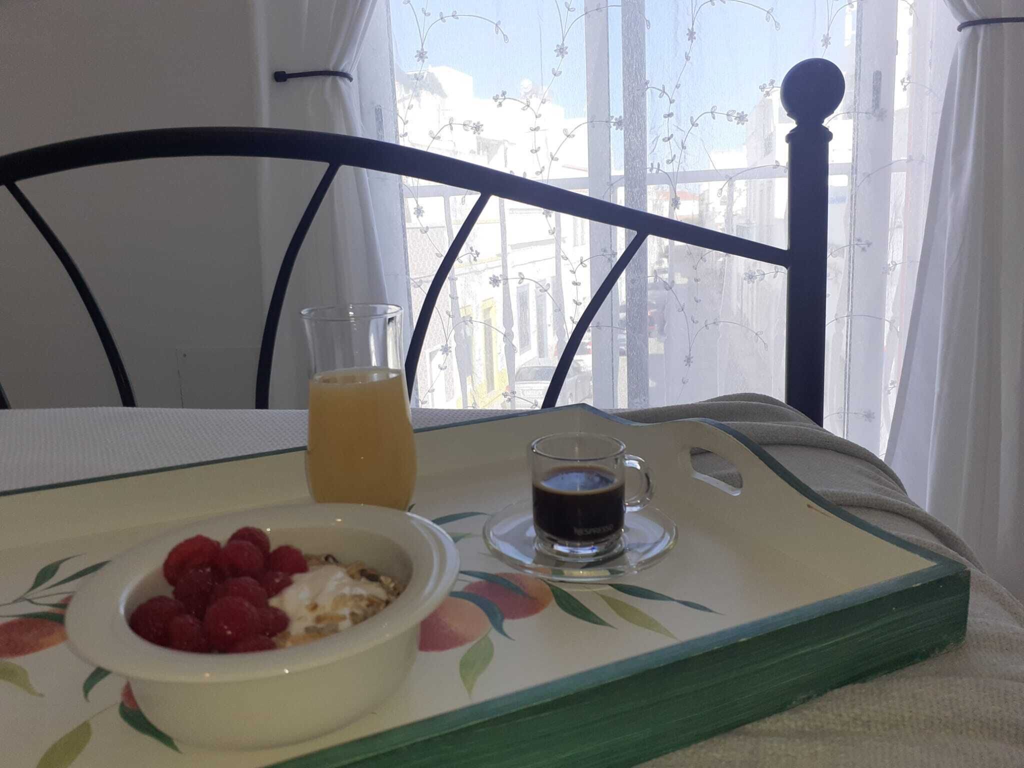 A breakfast tray with a bowl of raspberries, a glass of orange juice, and a cup of coffee on a table by a window with a view of buildings.
