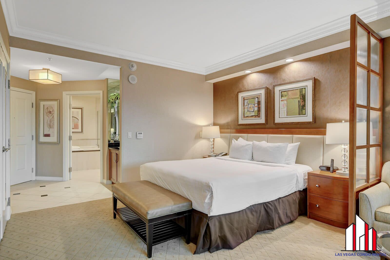 Quarto de hotel com uma cama grande, mesas de cabeceira, um banco e vista para o corredor.