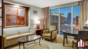 Une chambre d’hôtel dotée d’une grande fenêtre donnant sur la ville, d’un canapé, d’un fauteuil, d’une petite table et d’une lampe.
