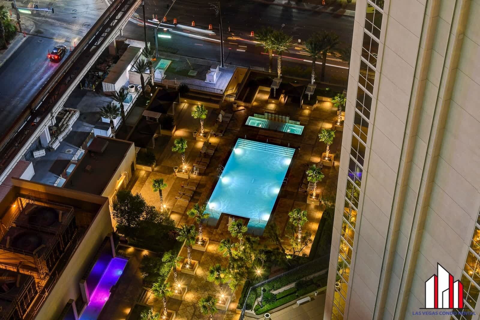 Vista aérea de un hotel con piscina, rodeado de mobiliario exterior y palmeras.