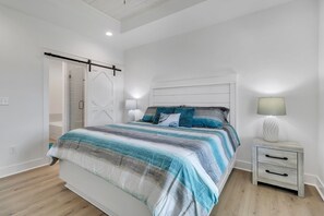 Relax in a serene bedroom with a large bed, striped bedspread, and a bedside table with a lamp.