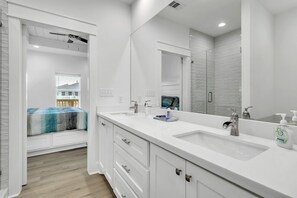 Features a sleek vanity with dual sinks and a large mirror, a walk-in shower with a glass door, and a bench.