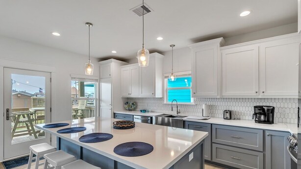A modern kitchen with white cabinets, a large island with stools, pendant lighting, and a view of the outside.
