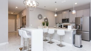Una cucina moderna con isola centrale, sgabelli da bar, elettrodomestici in acciaio inossidabile e illuminazione a sospensione.