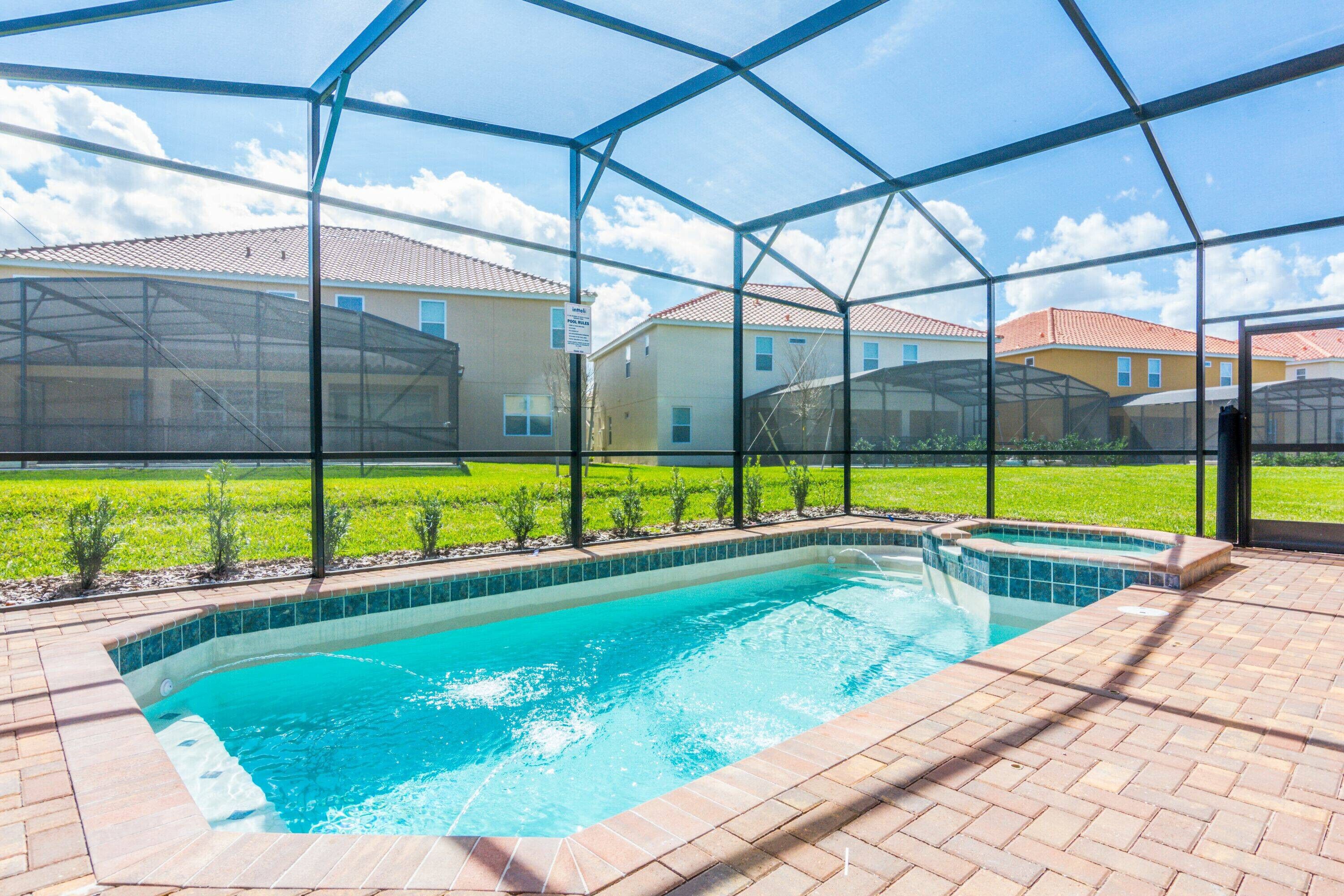 A swimming pool with a clear blue water, surrounded by a brick deck and enclosed by a glass structure.