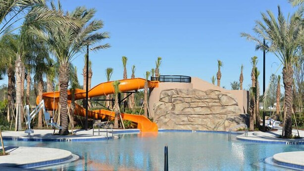 Ein Poolbereich mit Wasserrutsche, Palmen und Felsformationen im Hintergrund.