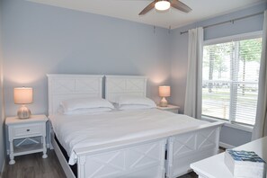 A bedroom with a white bed, two bedside tables with lamps, a ceiling fan, and a window with blinds. - Family fun-large home, beach, marina, pools (Long Neck)