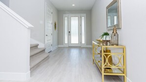Un couloir avec un escalier, une porte et une console ornée d’objets décoratifs.
