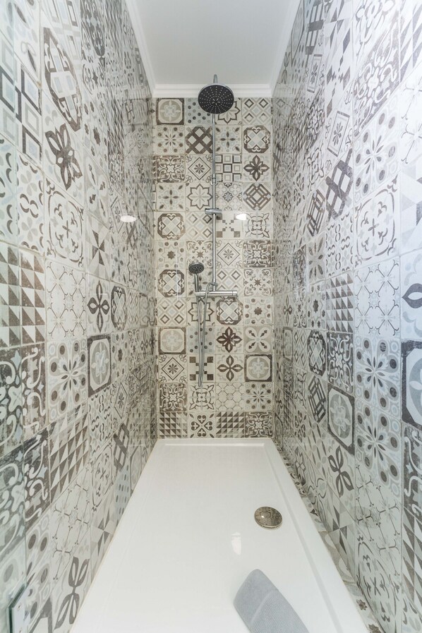 A shower area with a white floor and a showerhead. The walls are tiled with various geometric and floral patterns. - FLH Santa Cruz Triplex with Terrace (Santa Cruz)
