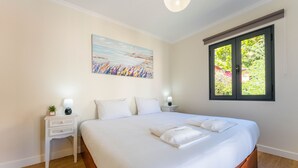Un dormitorio con una cama grande, dos mesitas de noche, una lámpara auxiliar, un cuadro y una ventana con vistas a zonas verdes.