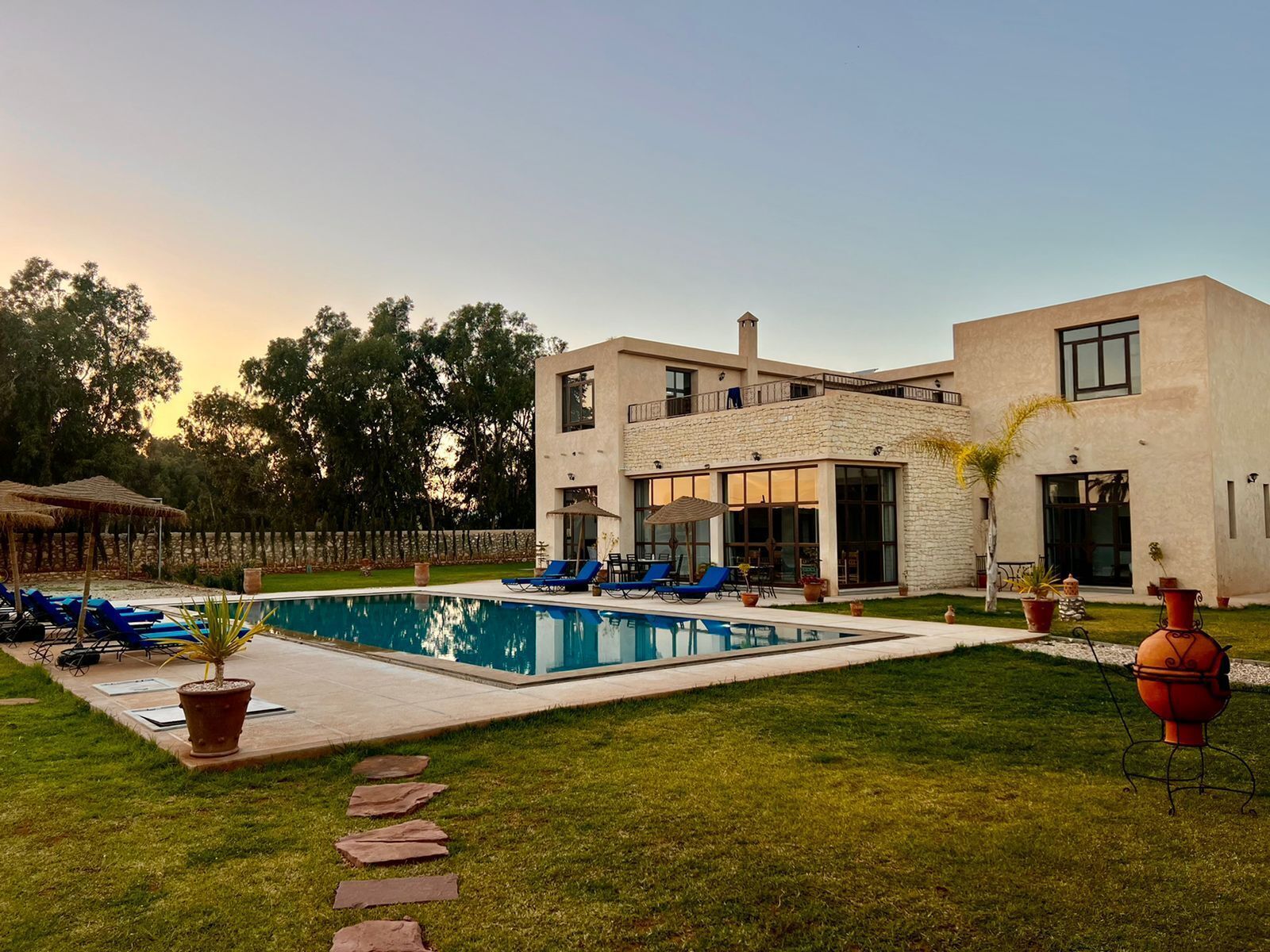 A modern two-story house with a swimming pool, outdoor seating, and a well-maintained lawn.