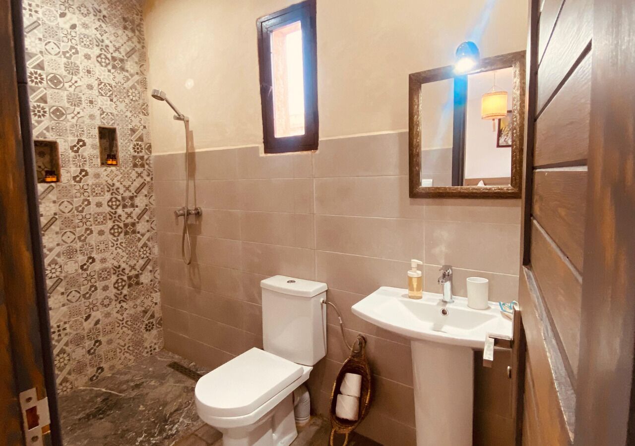 A bathroom with a patterned shower wall, a toilet, a sink with a mirror, and a towel rack.